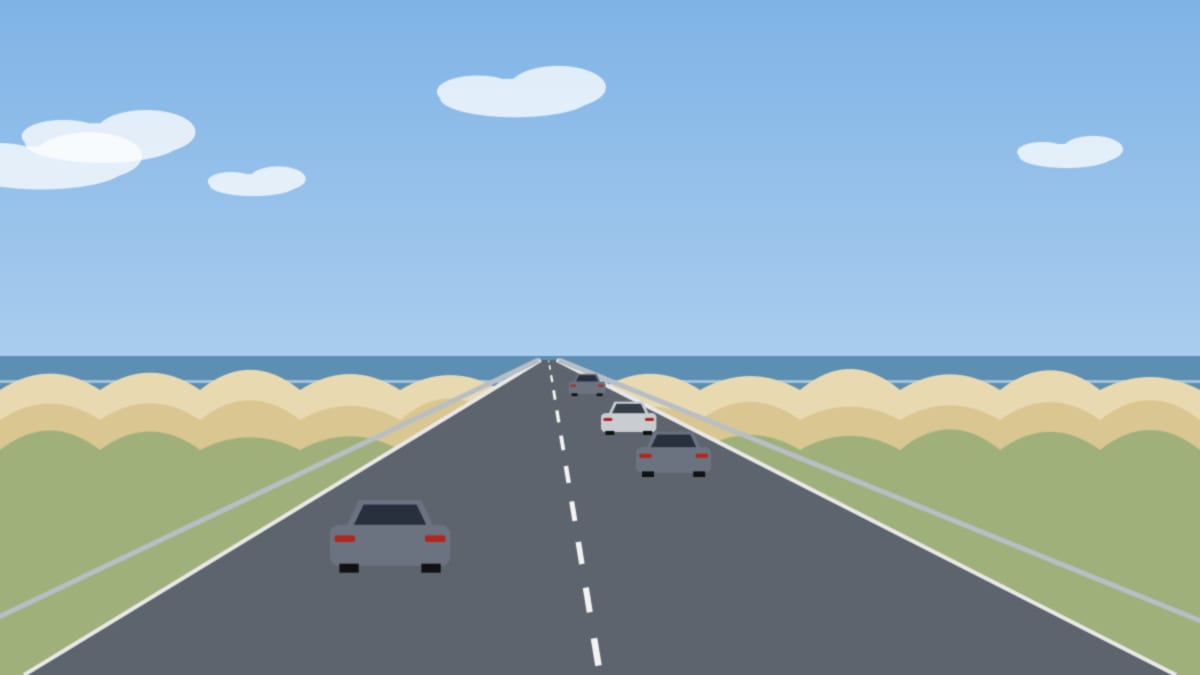 Straße an der Küste zwischen Dünen und Meer, im Hintergrund ein weiter Himmel mit Wolken
